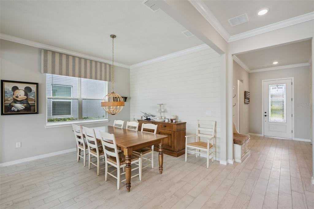 A dining room with a wooden table, white chairs, shiplap wall, and a globe pendant light — 13871 DESTIN BEACH LANE, ORLANDO, FL