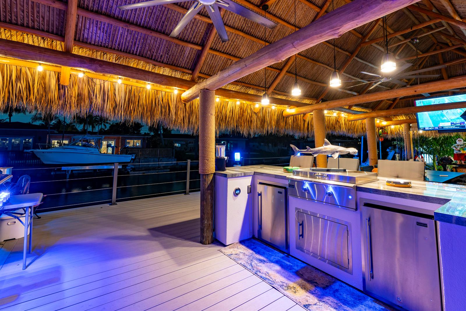 An outdoor kitchen with stainless steel appliances sits under a thatched roof overlooking a canal — 851 SE 5th Avenue, Pompano Beach FL 33060, POMPANO BEACH, FL