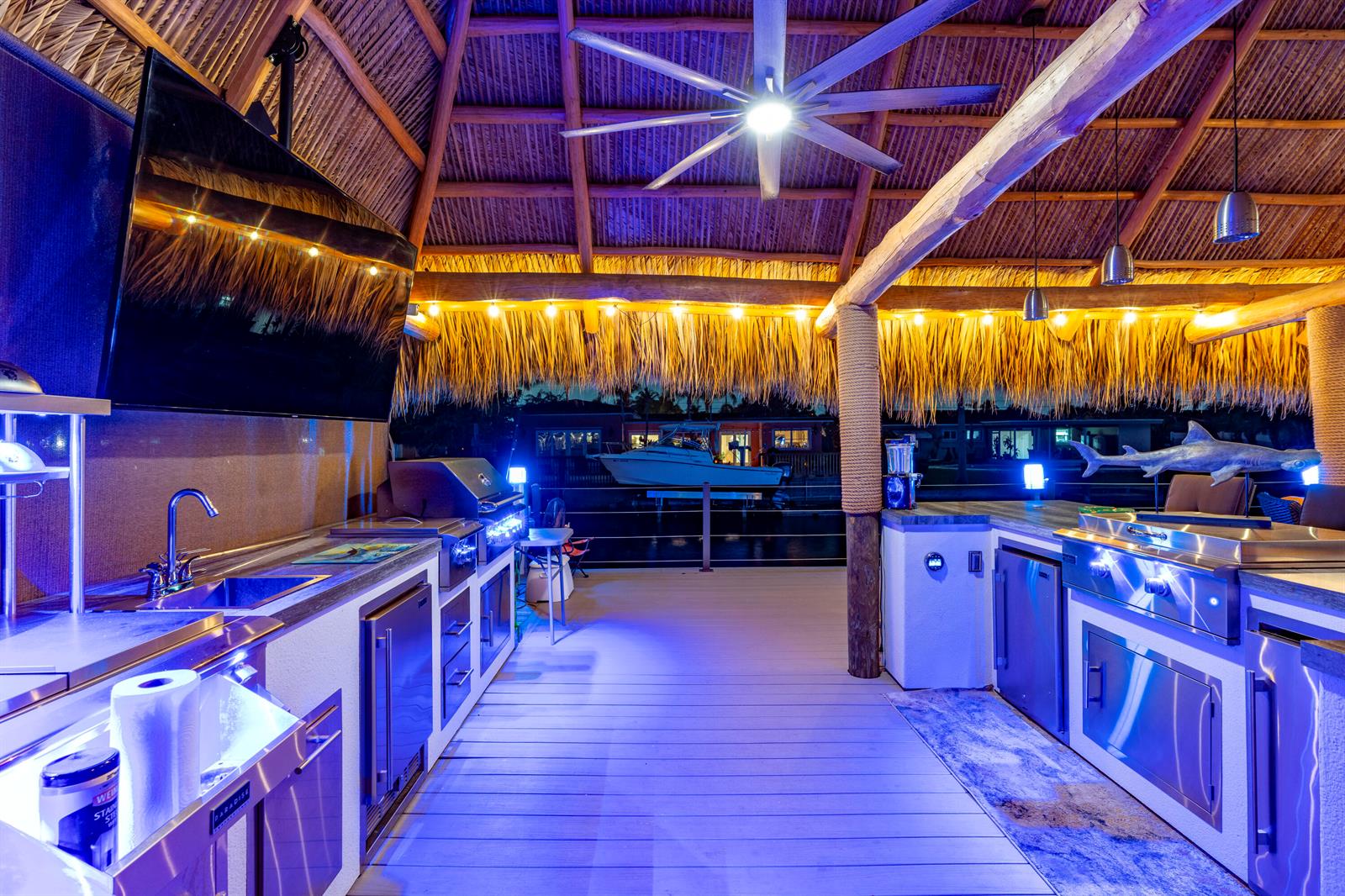An outdoor kitchen with stainless steel appliances under a thatched roof overlooking a boat dock — 851 SE 5th Avenue, Pompano Beach FL 33060, POMPANO BEACH, FL