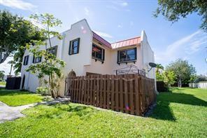 Exterior view of a two-story stucco townhouse with a wooden privacy fence and metal roof — 6363 Seven Springs Boulevard # A, FL 33463, FL