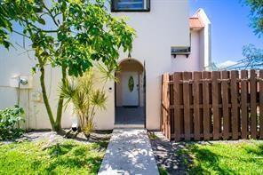 A white building exterior features a front entrance, a small tree, and a wooden fence — 6363 Seven Springs Boulevard # A, FL 33463, FL