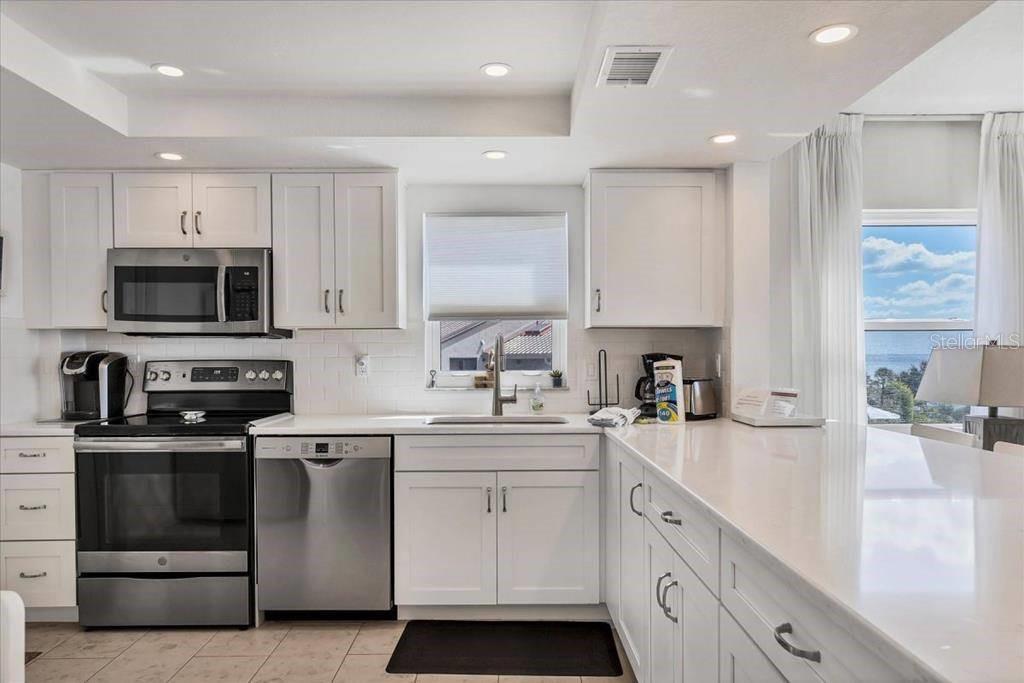 A bright kitchen features white cabinets, stainless steel appliances, quartz countertops, and a window view — 6154 MIDNIGHT PASS ROAD UNIT 301, SARASOTA, FL