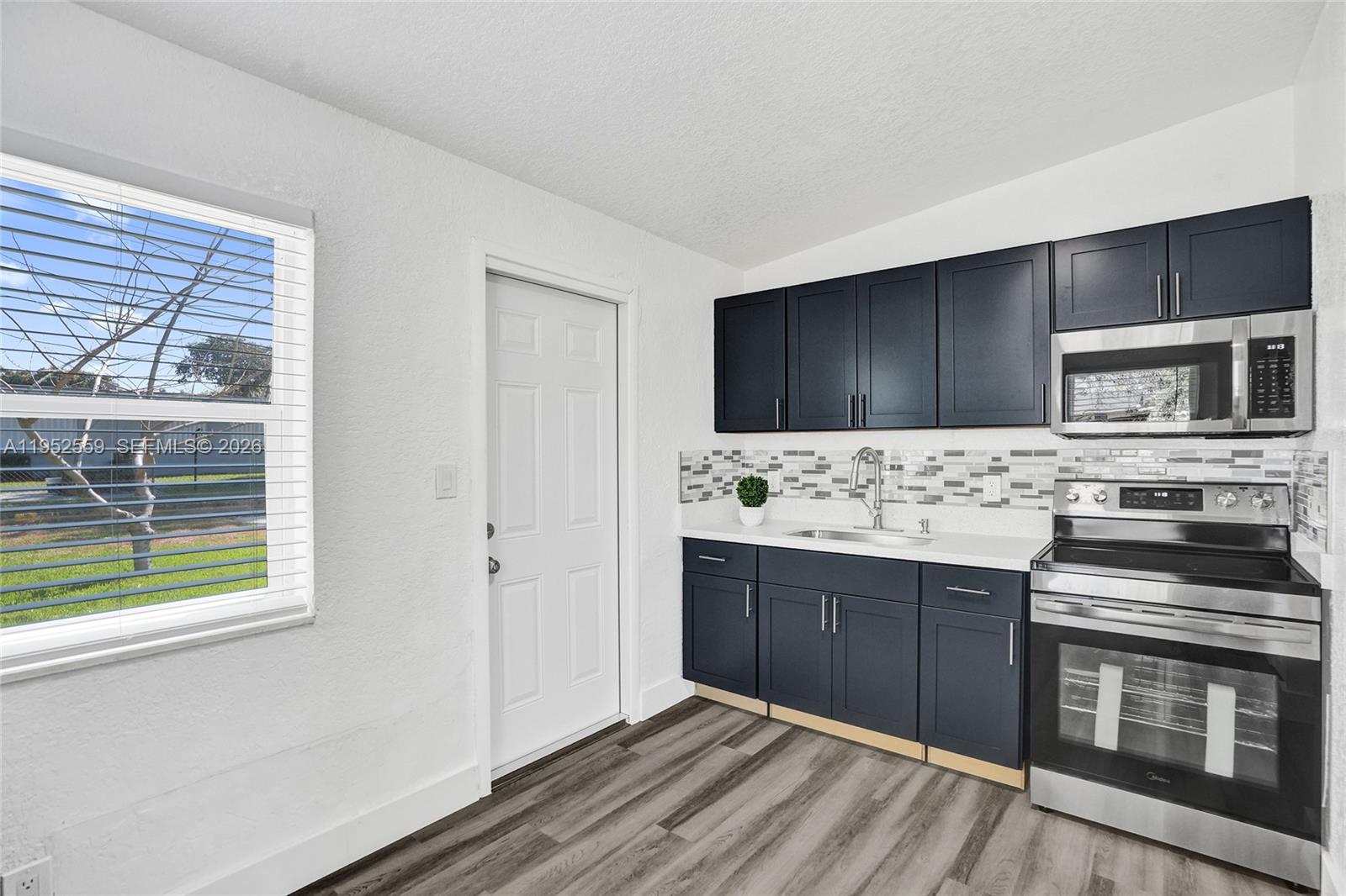 A kitchen features dark blue cabinets, stainless steel appliances, a tiled backsplash, and wood-look flooring — 1582 NW 5th Ave, Pompano Beach FL 33060, POMPANO BEACH, FL