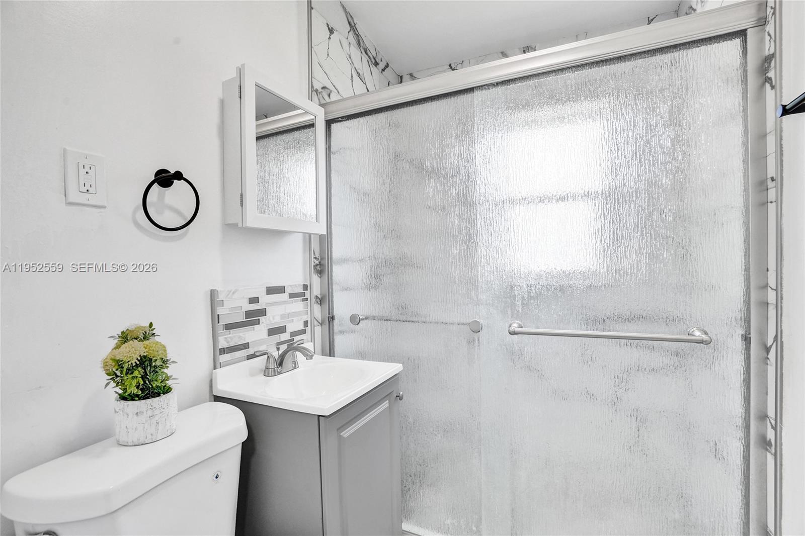 A bathroom features a gray vanity, a toilet, and a glass-enclosed shower with marble-patterned walls — 1582 NW 5th Ave, Pompano Beach FL 33060, POMPANO BEACH, FL