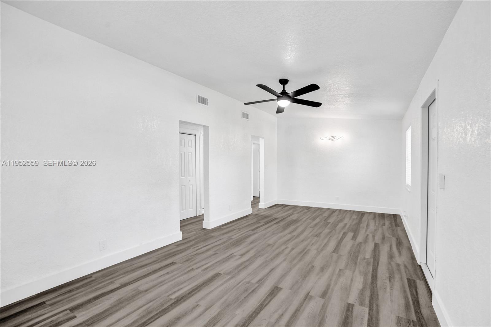 A bright, empty room features white walls, a ceiling fan, and gray wood-look flooring — 1582 NW 5th Ave, Pompano Beach FL 33060, POMPANO BEACH, FL