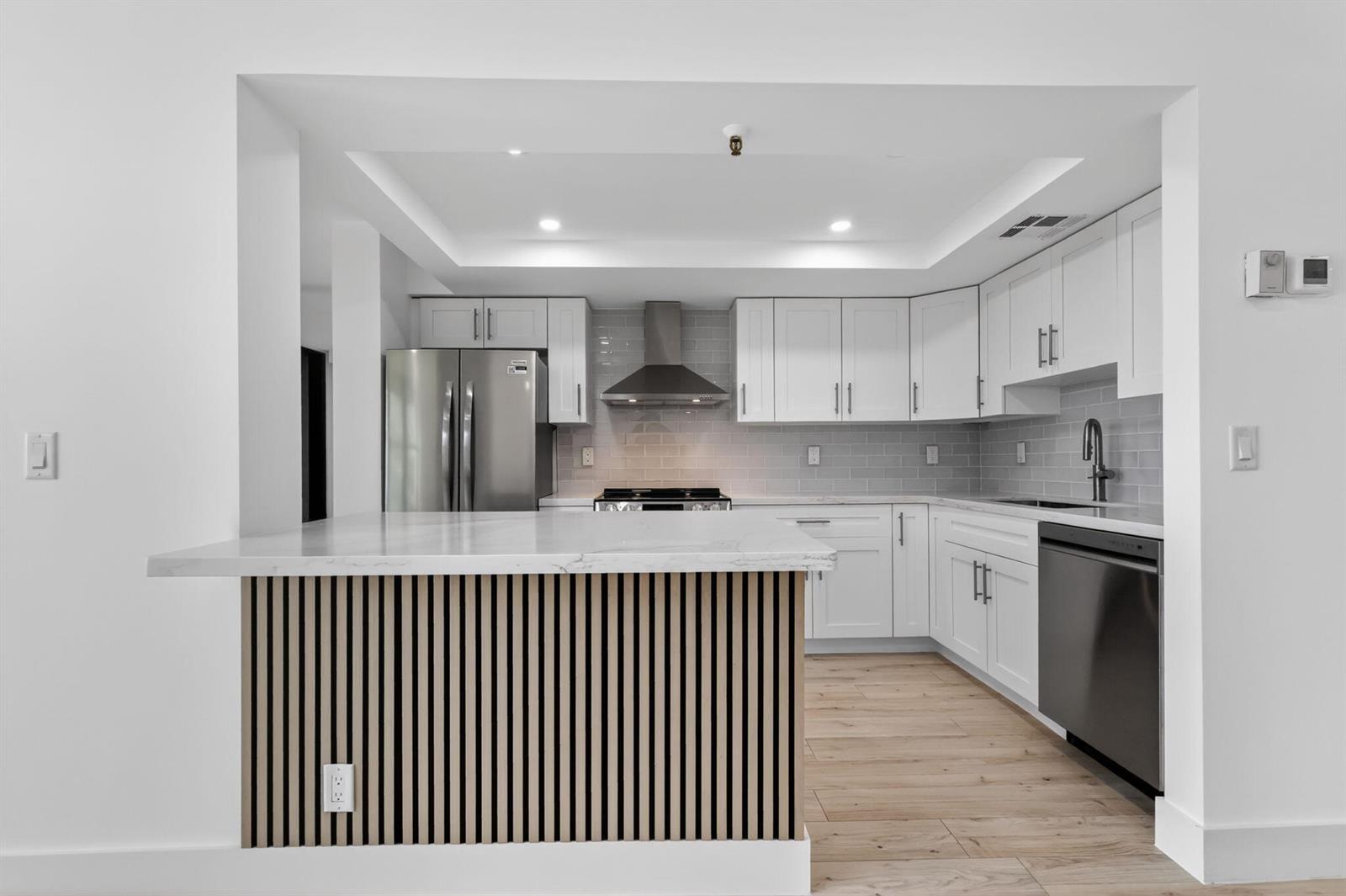 A modern kitchen features white cabinetry, stainless steel appliances, and a slatted wood kitchen island — 1748 Jupiter Cove Drive # 319, Jupiter FL 33469, JUPITER, FL