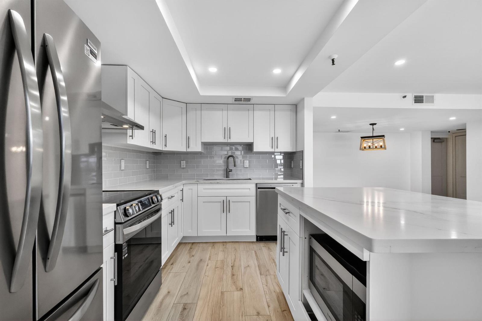 A modern kitchen features white cabinets, stainless steel appliances, a marble island, and wood-look flooring — 1748 Jupiter Cove Drive # 319, Jupiter FL 33469, JUPITER, FL
