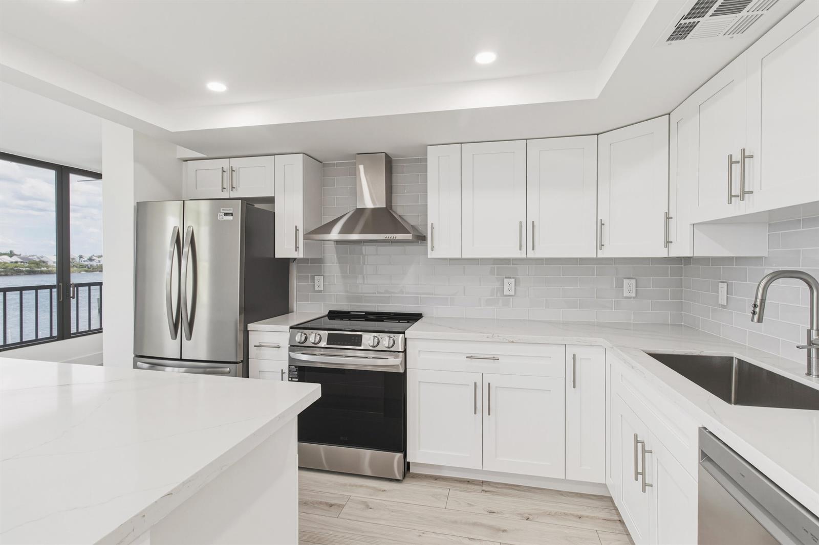 A modern kitchen features white cabinets, stainless steel appliances, quartz countertops, and a water view — 1748 Jupiter Cove Drive # 319, Jupiter FL 33469, JUPITER, FL