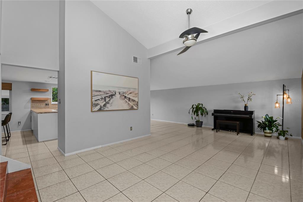 A spacious living area features light-colored tile flooring, a vaulted ceiling, and a black piano — 1304 ORTEGA STREET, WINTER SPRINGS, FL