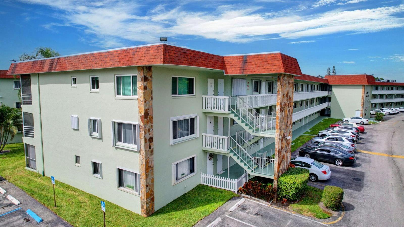 An exterior view of a multi-story apartment building with green stucco walls and red roofs — 3200 Springdale Boulevard # 217, Palm Springs FL 33461, PALM SPRINGS, FL