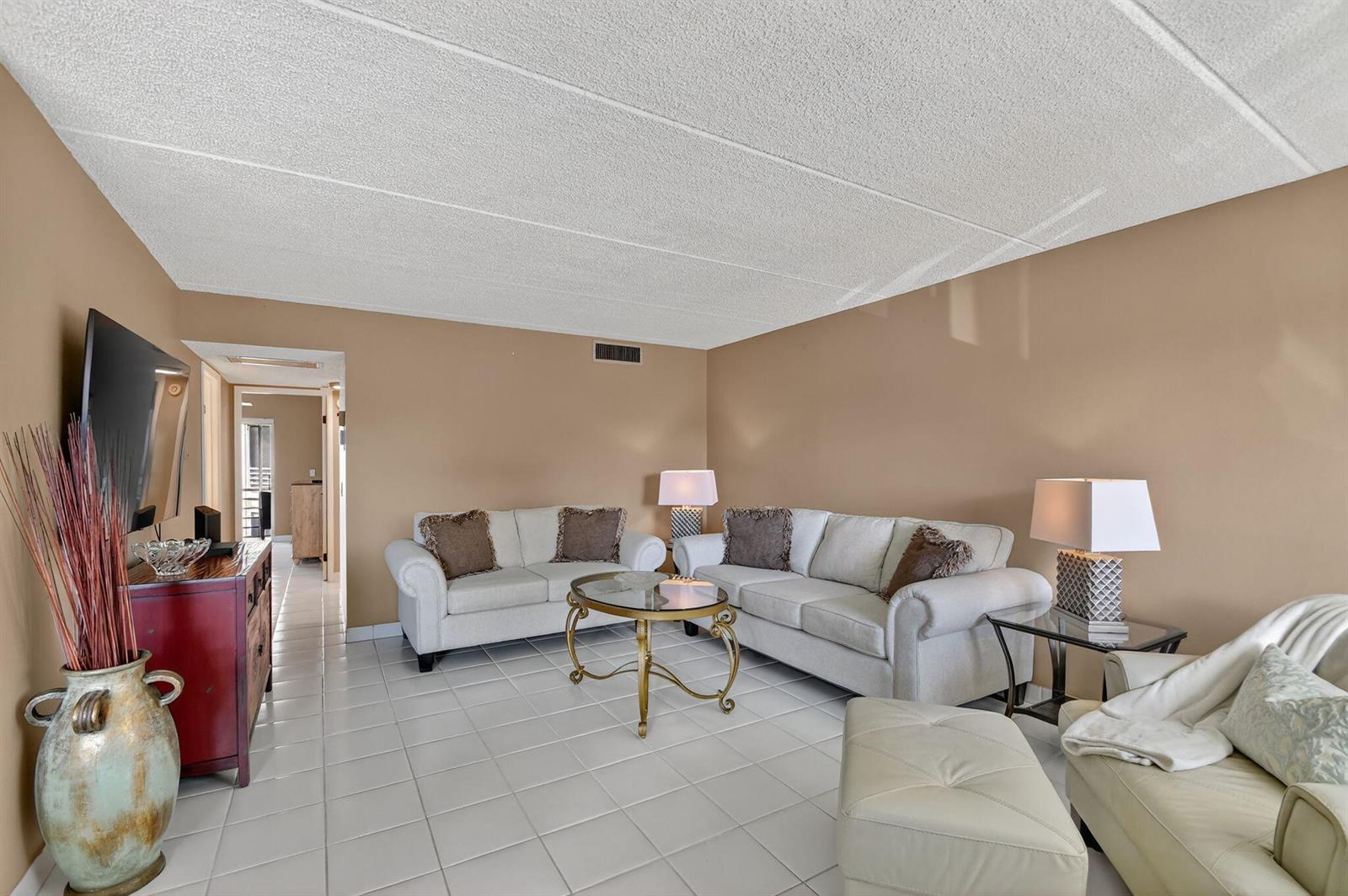 A living room features white tile floors, beige walls, two sofas, and a glass coffee table — 3200 Springdale Boulevard # 217, Palm Springs FL 33461, PALM SPRINGS, FL