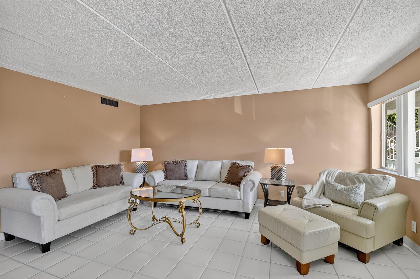 A living room features white tile floors, two sofas, an armchair with ottoman, and lamps — 3200 Springdale Boulevard # 217, Palm Springs FL 33461, PALM SPRINGS, FL