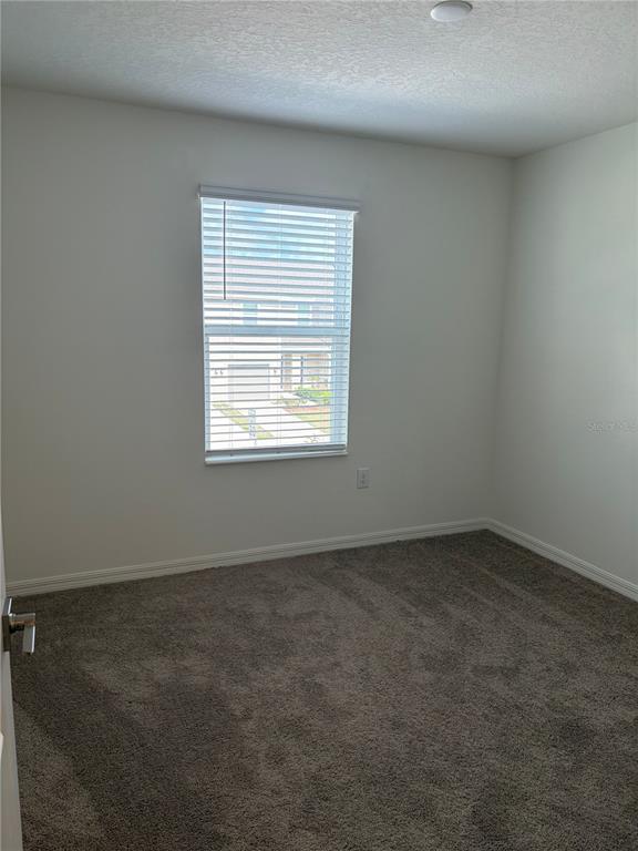 An empty bedroom features light-colored walls, gray carpeting, and a window with white blinds — 1492 MIRABELLA CIRCLE, DAVENPORT, FL