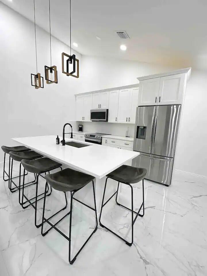 A modern kitchen features white cabinetry, a large island with bar seating, and marble flooring — 1255 Periwinkle Place, Wellington FL 33414, WELLINGTON, FL