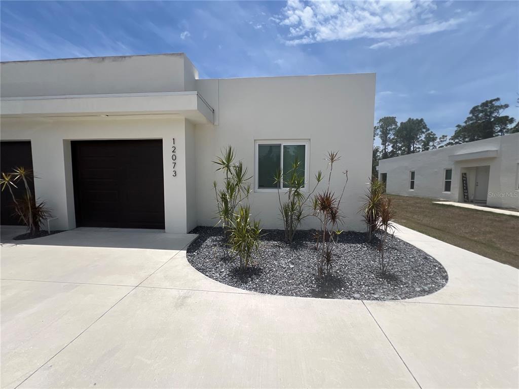 A modern, single-story white stucco home with a dark garage door and gravel landscaping — 12073 HENLEY AVENUE, PORT CHARLOTTE, FL