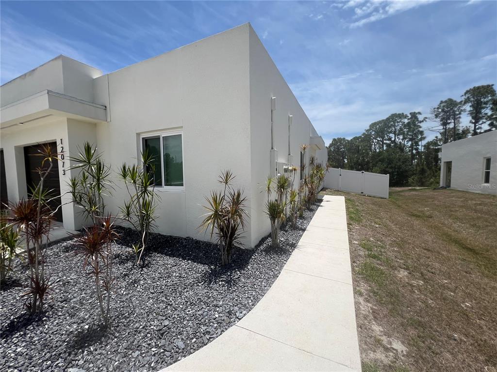 A white modern house exterior features a gravel garden bed and a concrete walkway — 12073 HENLEY AVENUE, PORT CHARLOTTE, FL