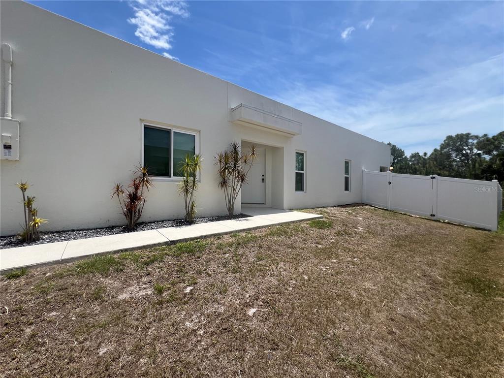 A white, flat-roofed house features a front walkway, sparse landscaping, and a white vinyl fence — 12073 HENLEY AVENUE, PORT CHARLOTTE, FL
