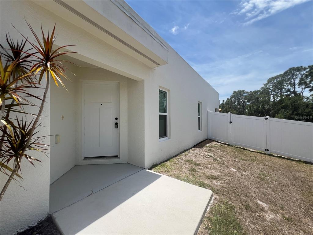 A white exterior wall features a front door, a concrete porch, and a vinyl fence — 12073 HENLEY AVENUE, PORT CHARLOTTE, FL