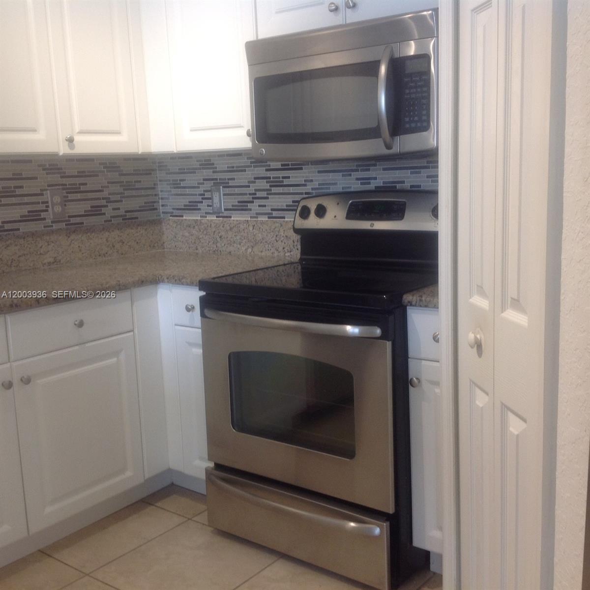 A kitchen features white cabinets, stainless steel appliances, granite countertops, and a tiled backsplash — 11401 NW 89th St # 105, Doral FL 33178, DORAL, FL