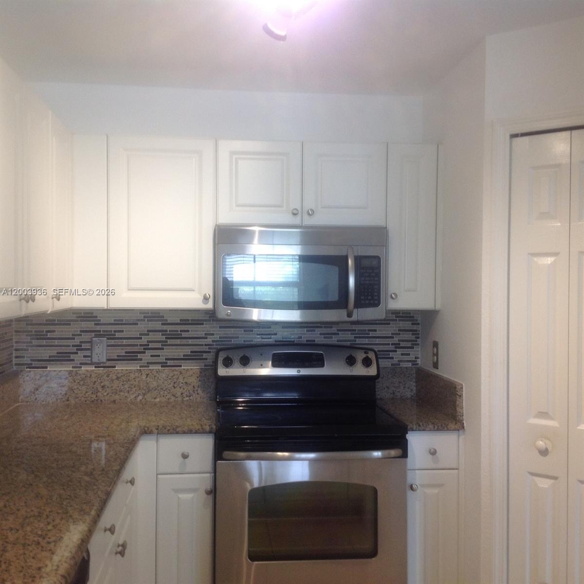 A kitchen features white cabinets, stainless steel appliances, granite countertops, and a tiled backsplash — 11401 NW 89th St # 105, Doral FL 33178, DORAL, FL