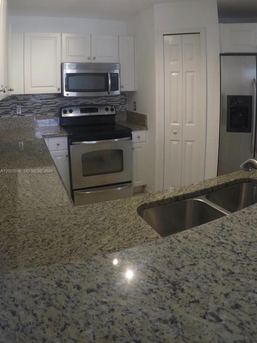 A kitchen features white cabinets, granite countertops, stainless steel appliances, and a double sink — 11401 NW 89th St # 105, Doral FL 33178, DORAL, FL