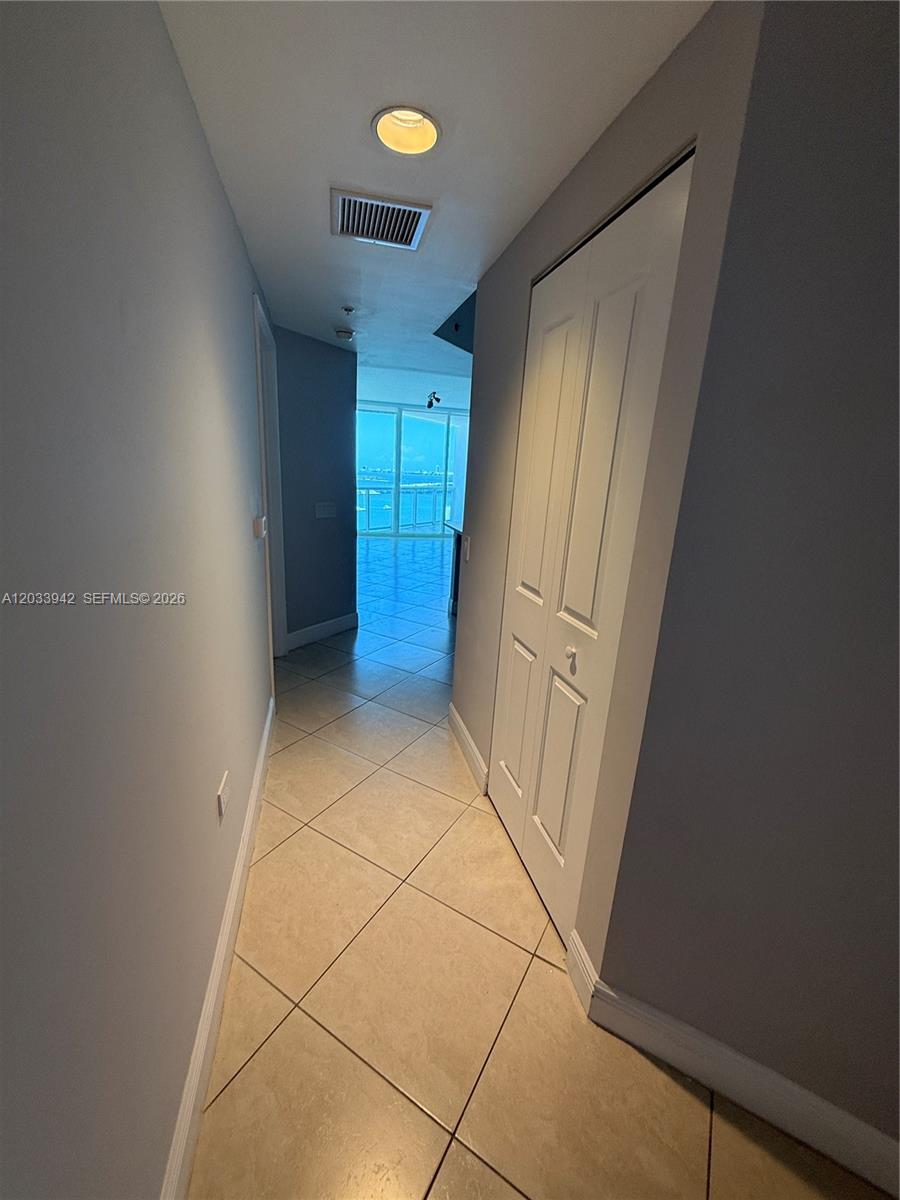 A hallway with light-colored tile floors leads toward a room with floor-to-ceiling windows — 480 NE 30th St # 1504, Miami FL 33137, MIAMI, FL
