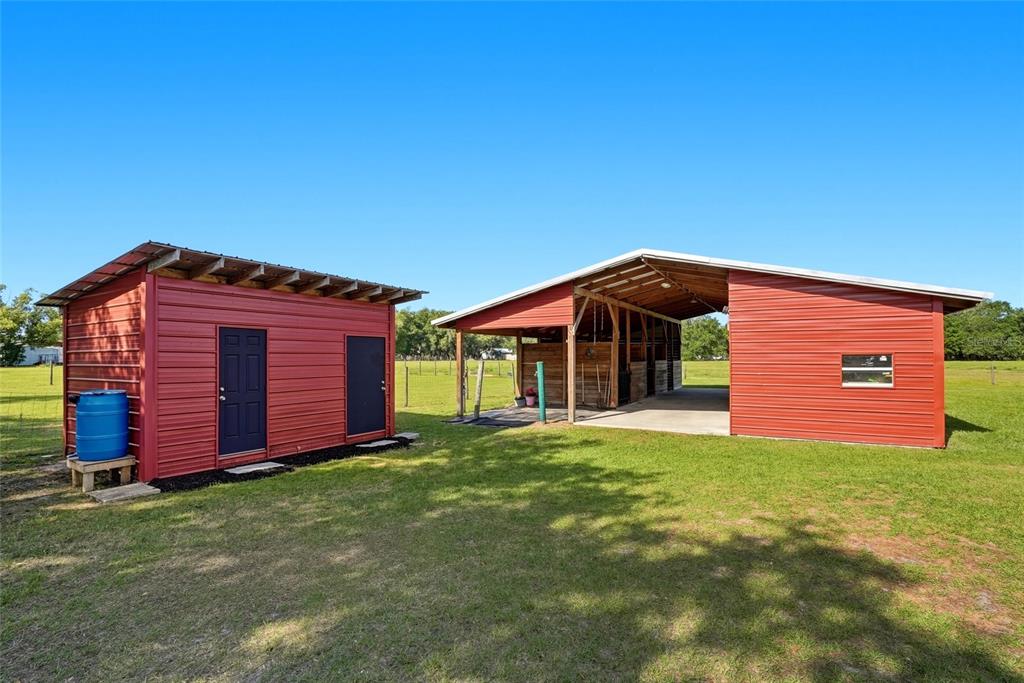 A red metal shed stands next to a matching open-air horse barn on a lawn — 123 S WIGGINS ROAD, PLANT CITY, FL