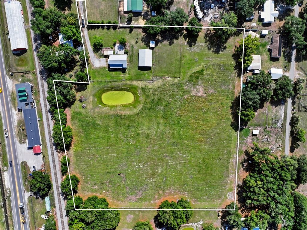 An aerial view shows a large, fenced grassy lot with a small pond and buildings — 123 S WIGGINS ROAD, PLANT CITY, FL