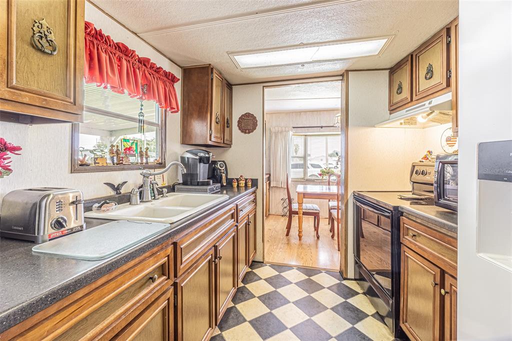 A kitchen with wood cabinets, black countertops, and a black and white checkered floor — 37544 ATTICA AVENUE, ZEPHYRHILLS, FL