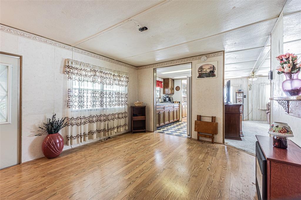 A living room with wood flooring, a large window with curtains, and an adjacent kitchen — 37544 ATTICA AVENUE, ZEPHYRHILLS, FL