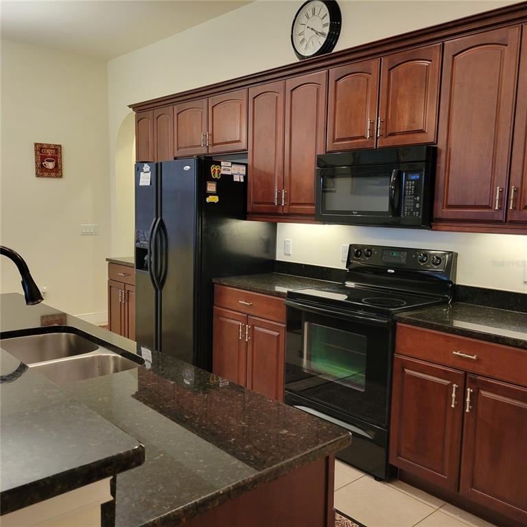 A kitchen features dark wood cabinets, black appliances, and dark granite countertops — 106 LERIDA COURT, NOKOMIS, FL