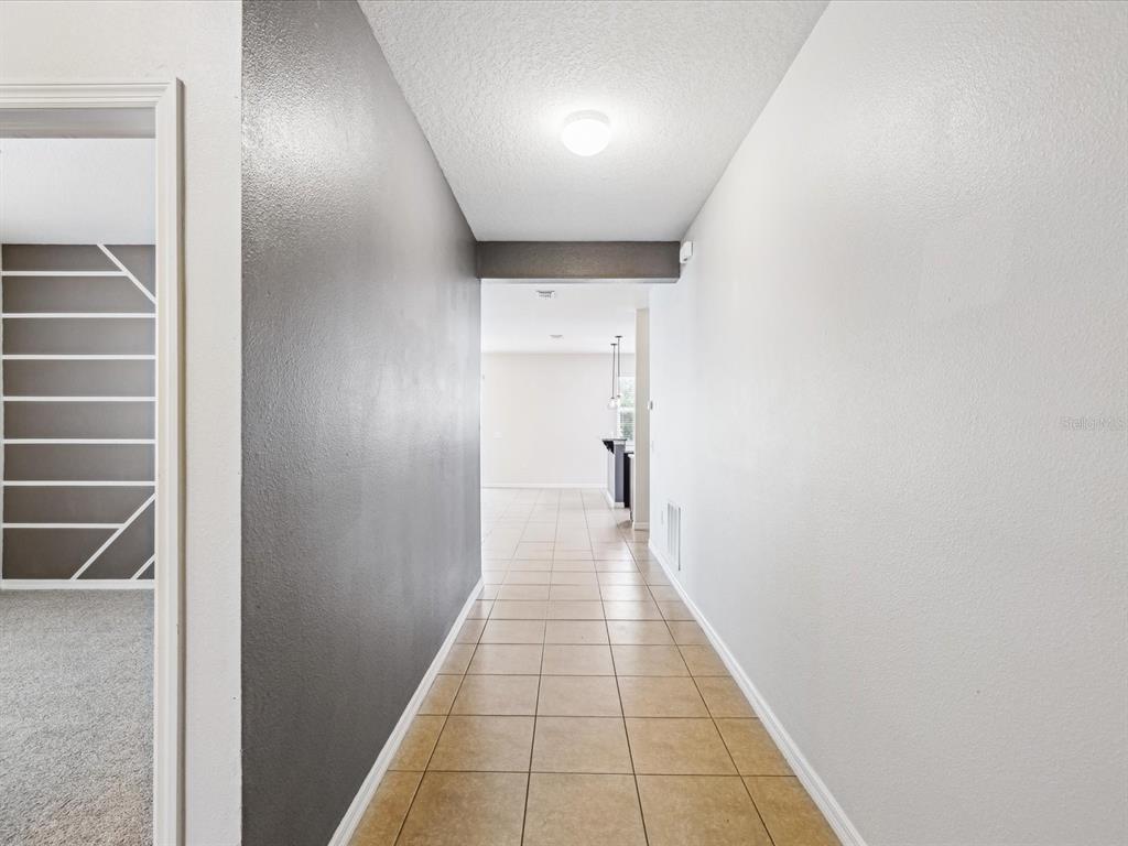 A hallway with tan tile flooring leads from a dark-accented wall toward an open kitchen — 11525 SOUTHERN CREEK DRIVE, GIBSONTON, FL