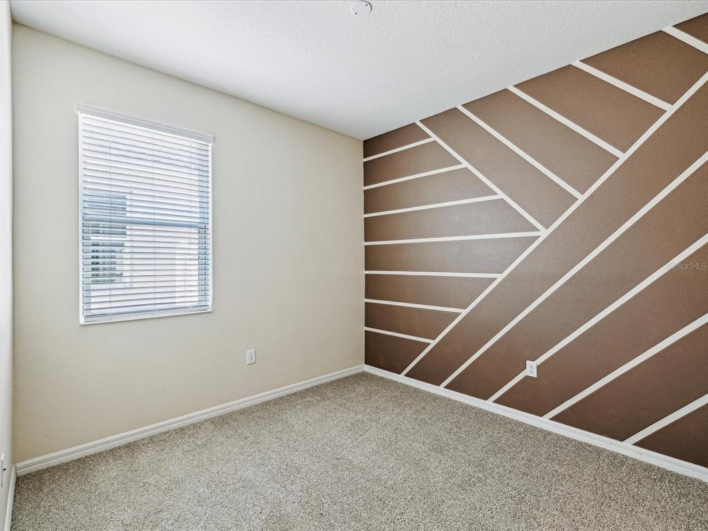 An empty bedroom features beige walls, carpeted flooring, and an accent wall with geometric molding — 11525 SOUTHERN CREEK DRIVE, GIBSONTON, FL