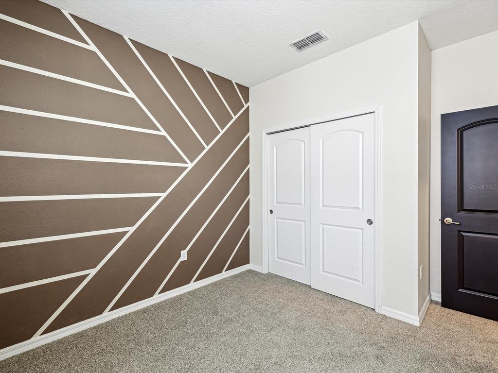 A bedroom features a brown accent wall with white geometric stripes, carpeted flooring, and white doors — 11525 SOUTHERN CREEK DRIVE, GIBSONTON, FL