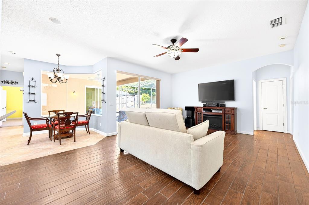 A living room with wood-look tile floors, a beige sofa, and an adjacent dining area — 270 VIA RUSSO LANE, LAKE MARY, FL