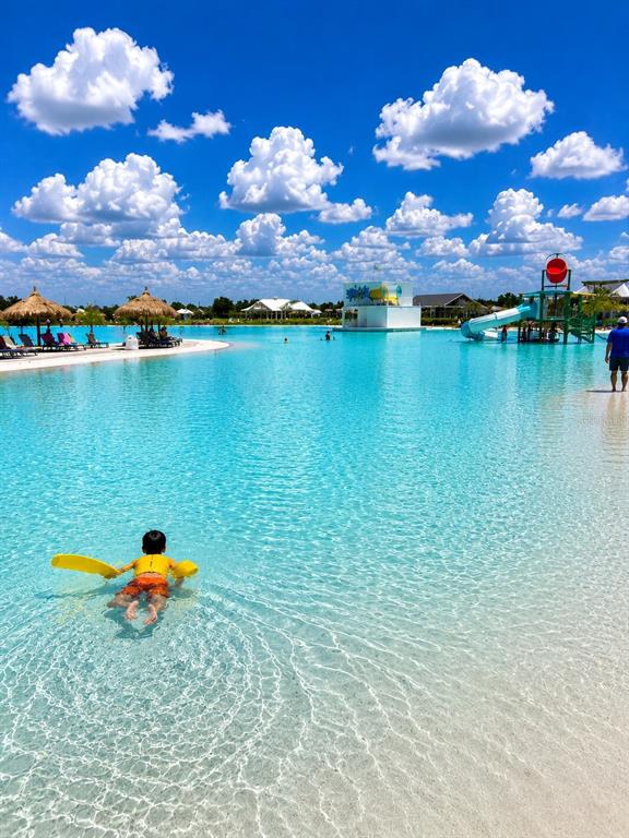 A child swims in a large, clear blue lagoon with a water slide and umbrellas — 10308 FIELDSTONE MYRTLE WAY, SAN ANTONIO, FL
