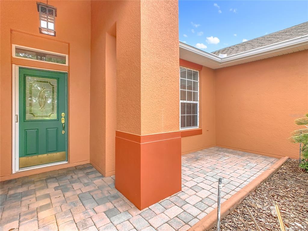 A paved entryway features a green front door and a large orange stucco pillar — 525 SHOREHAVEN  DRIVE, POINCIANA, FL