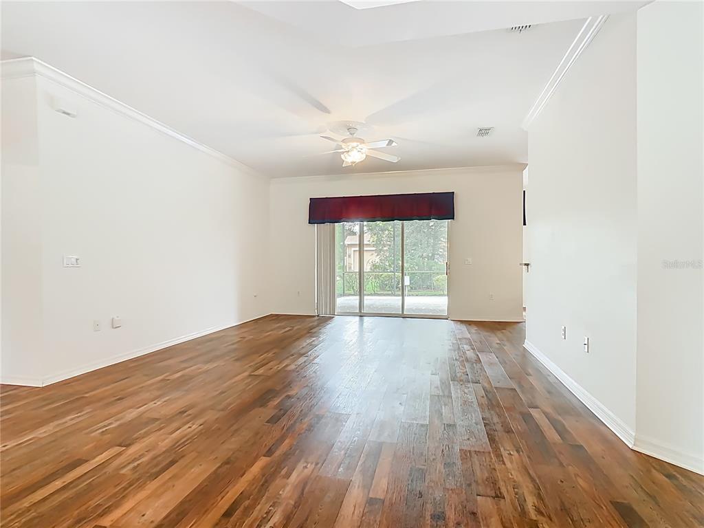 A spacious living room features hardwood flooring, a ceiling fan, and sliding glass patio doors — 525 SHOREHAVEN  DRIVE, POINCIANA, FL