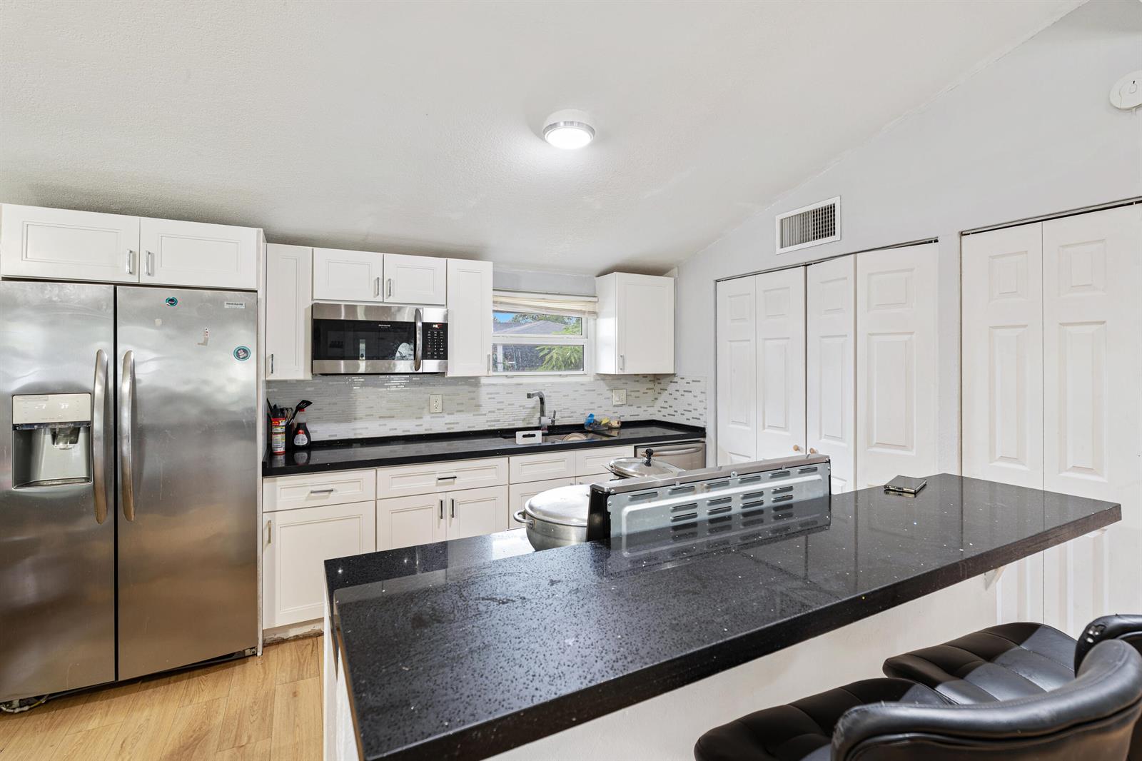A kitchen features white cabinets, black countertops, stainless steel appliances, and a breakfast bar — 3872 Mackinac Road, FL 33462, FL