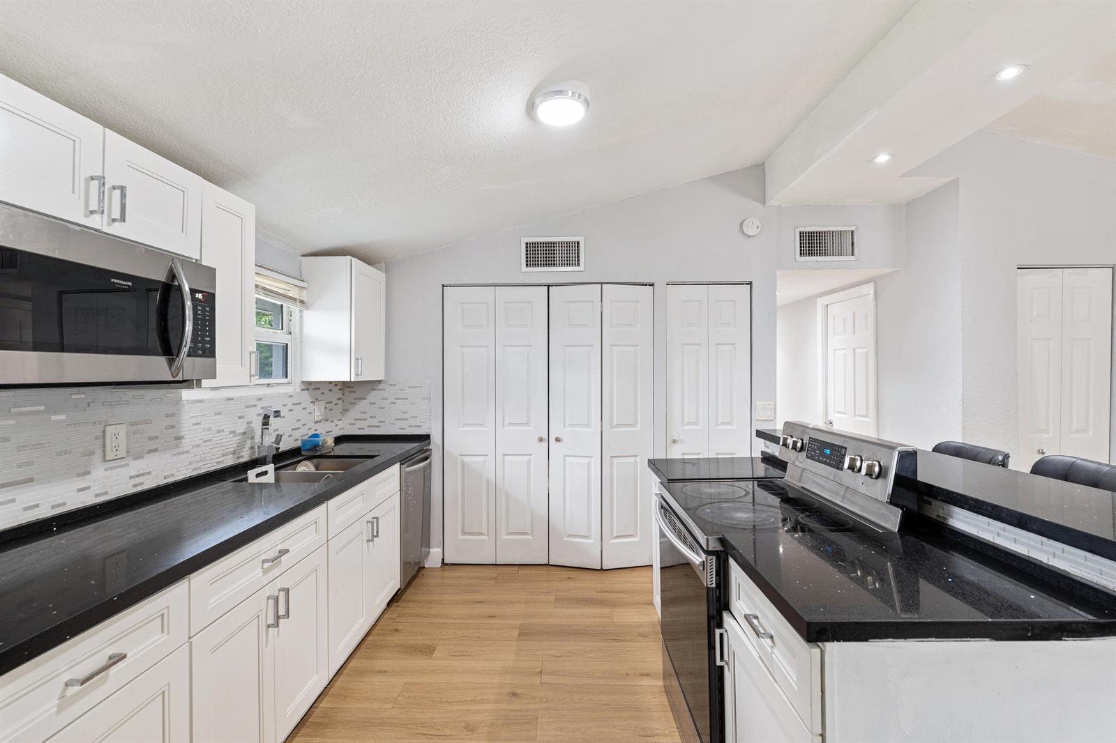 A kitchen features white cabinets, black countertops, stainless steel appliances, and light wood flooring — 3872 Mackinac Road, FL 33462, FL