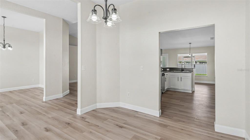 A dining area with light wood-look flooring leads into a kitchen with white cabinets — 530 BUCKSHOT LANE, LAKELAND, FL