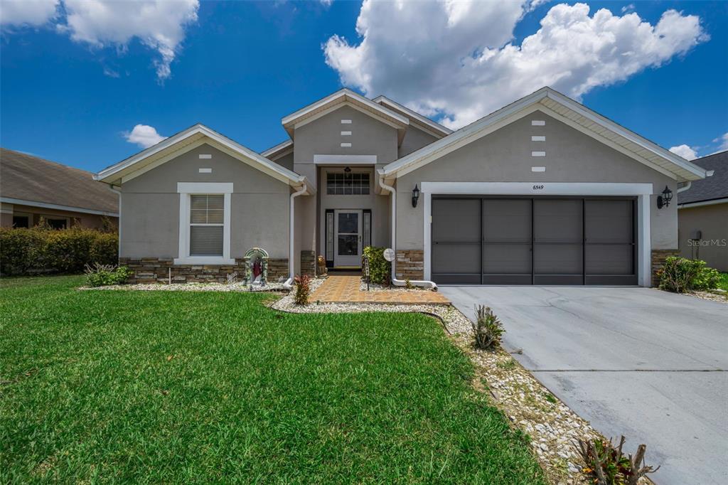 A single-story house with a gray stucco exterior, stone accents, and a two-car garage — 6549 CRESCENT LOOP, WINTER HAVEN, FL