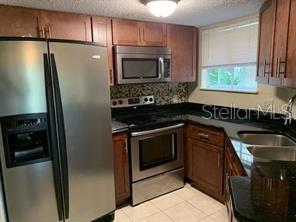 A kitchen features stainless steel appliances, dark wood cabinets, and a patterned tile backsplash — 1948 LAKE ATRIUMS CIRCLE UNIT 115, ORLANDO, FL
