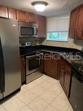 A kitchen features stainless steel appliances, dark wood cabinets, black countertops, and light tile flooring — 1948 LAKE ATRIUMS CIRCLE UNIT 115, ORLANDO, FL