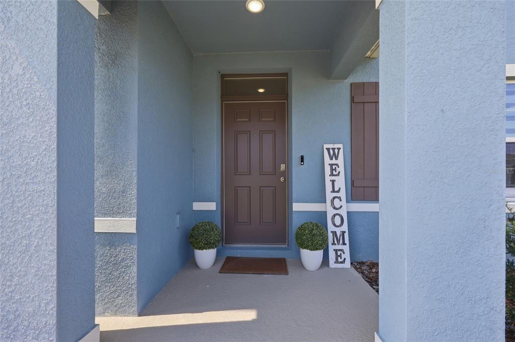 A covered front porch features a brown door, a welcome sign, and two potted plants — 3719 PARAGON LANE, CLERMONT, FL