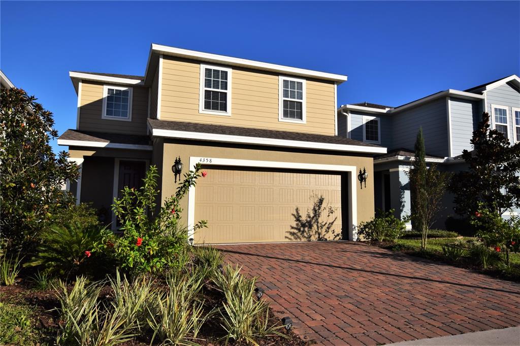 A two-story house with tan siding, a brick driveway, and a two-car garage — 4358 SILVER CREEK STREET, KISSIMMEE, FL