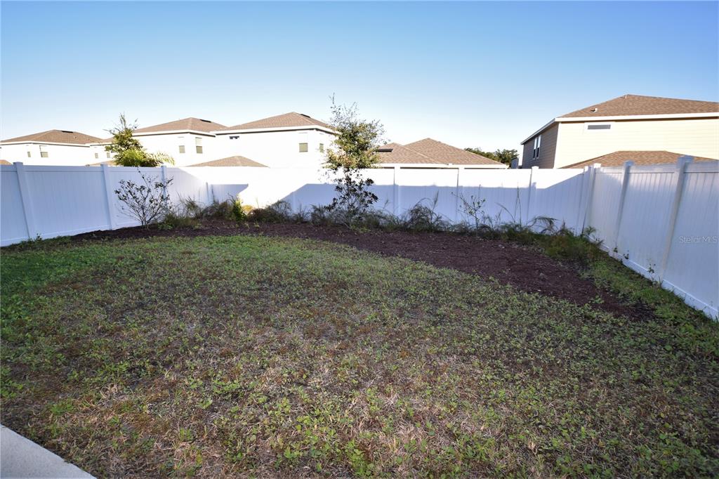 A fenced backyard features a patch of grass and a mulched area with small shrubs — 4358 SILVER CREEK STREET, KISSIMMEE, FL