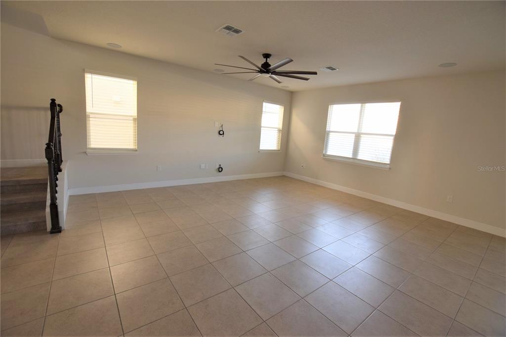 A spacious, empty living room features light-colored tile flooring, a ceiling fan, and multiple windows — 4358 SILVER CREEK STREET, KISSIMMEE, FL
