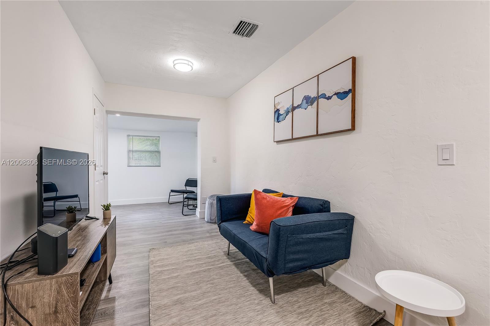 A living room features a blue sofa, a television on a stand, and light flooring — 327 NE 55th St # 2, Miami FL 33137, MIAMI, FL