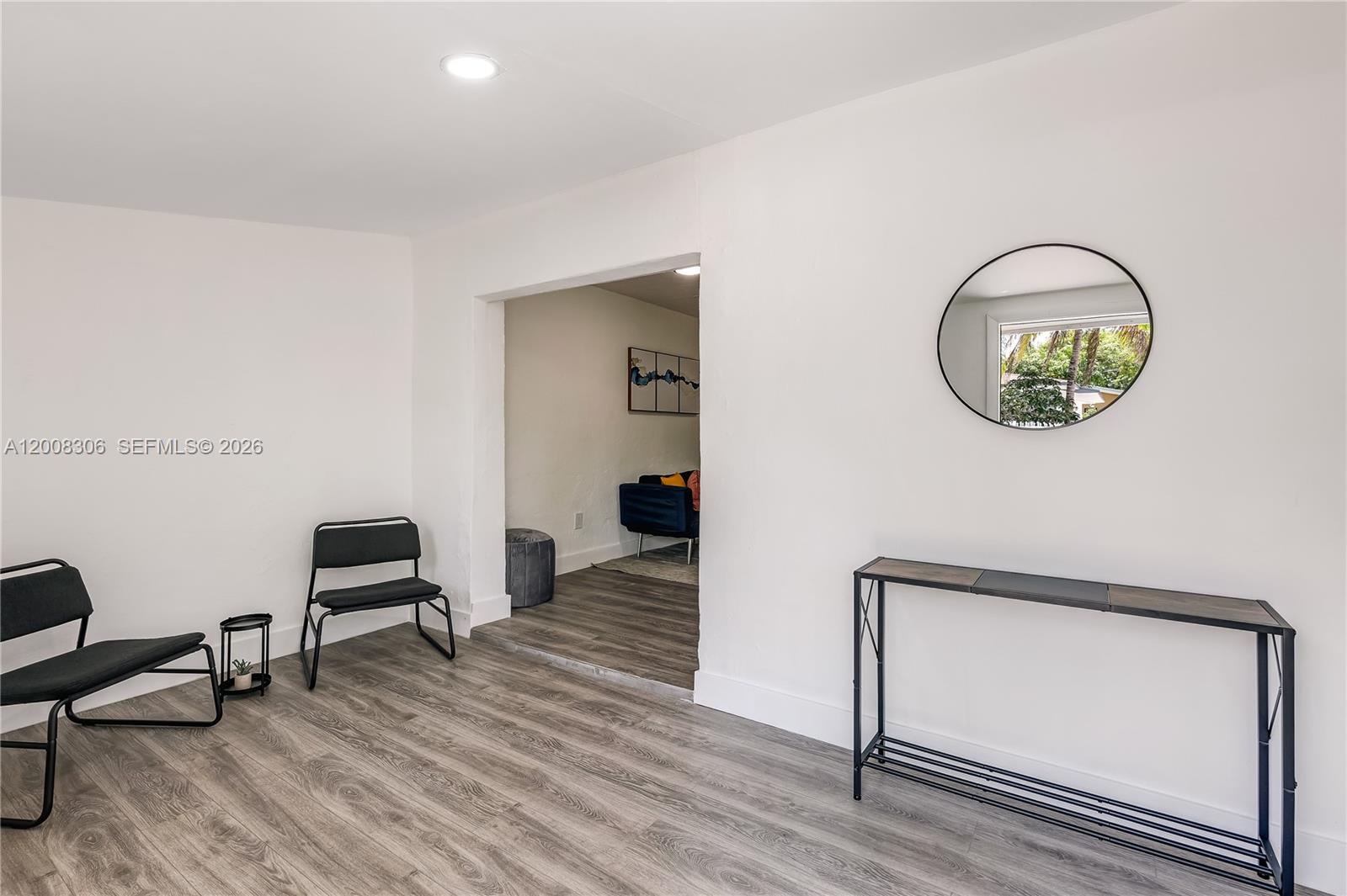 A minimalist room features wood-look flooring, two black chairs, a console table, and a mirror — 327 NE 55th St # 2, Miami FL 33137, MIAMI, FL